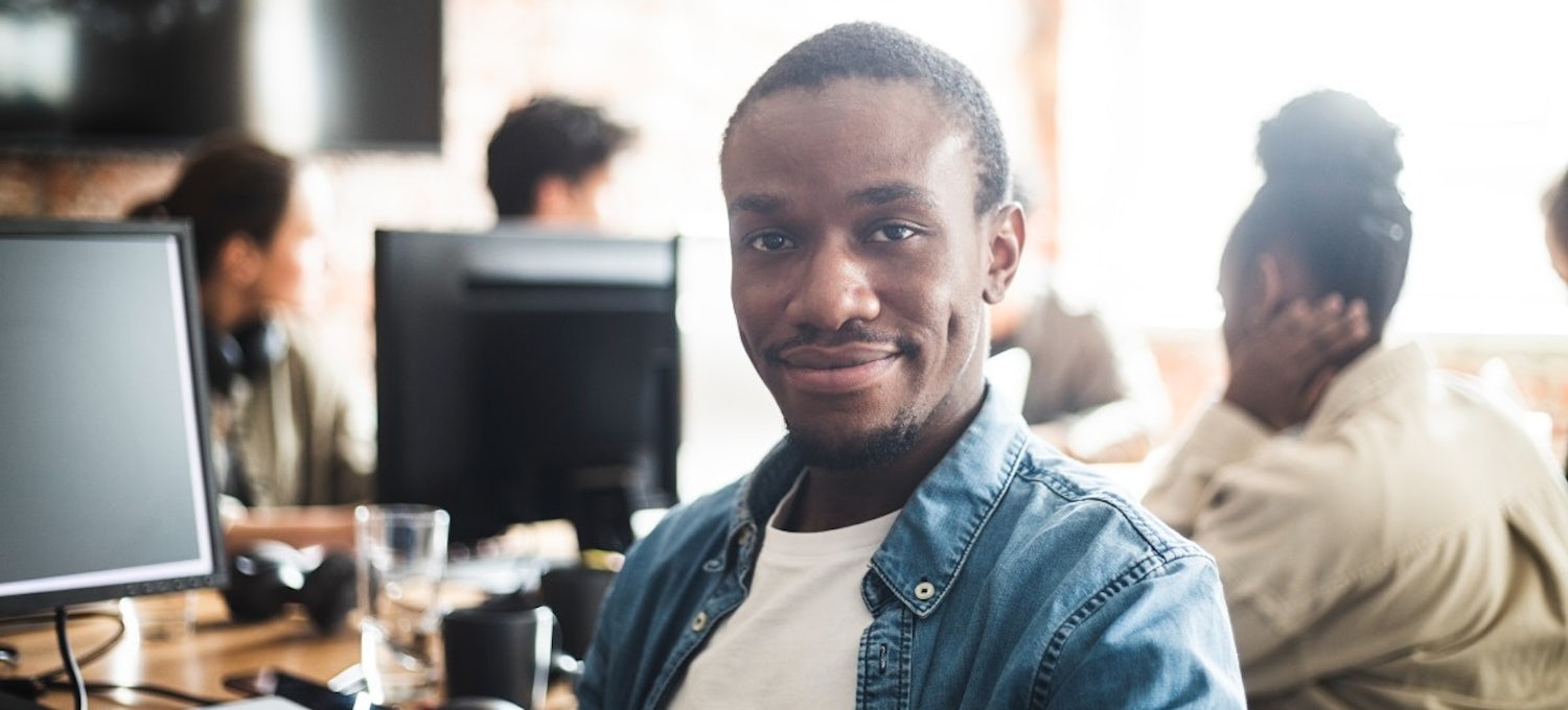 [Featured image] An employee wearing a white t-shirt under a blue denim button-down smiles during an employee development training class.