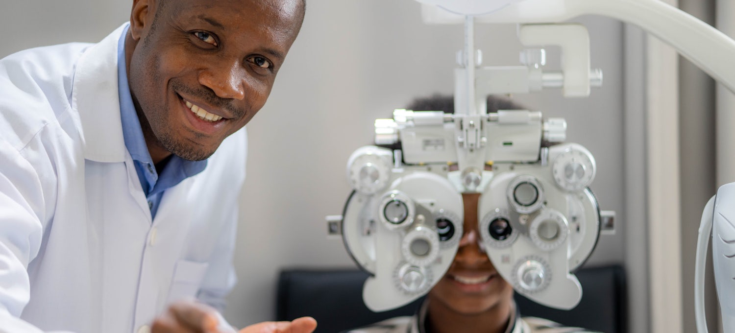 [Featured Image] An optician in a white lab coat gives a patient an eye exam.