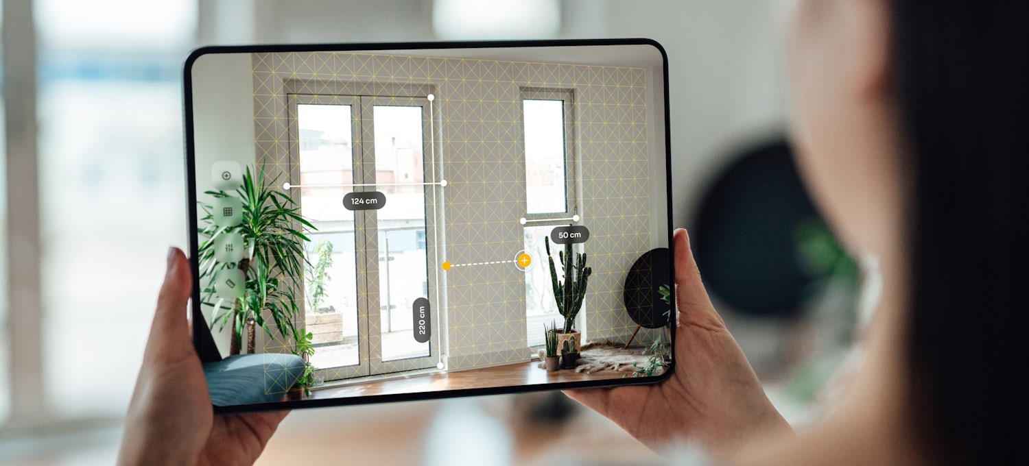 [Featured image] A woman uses an augmented reality app on a tablet to measure space for her interior design career. 