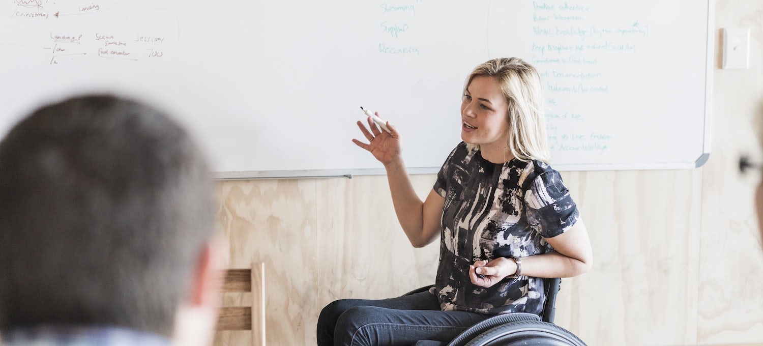 [Imagen destacada] Un diseñador de UX en silla de ruedas trabaja en un reto de whiteboard durante una entrevista de trabajo.