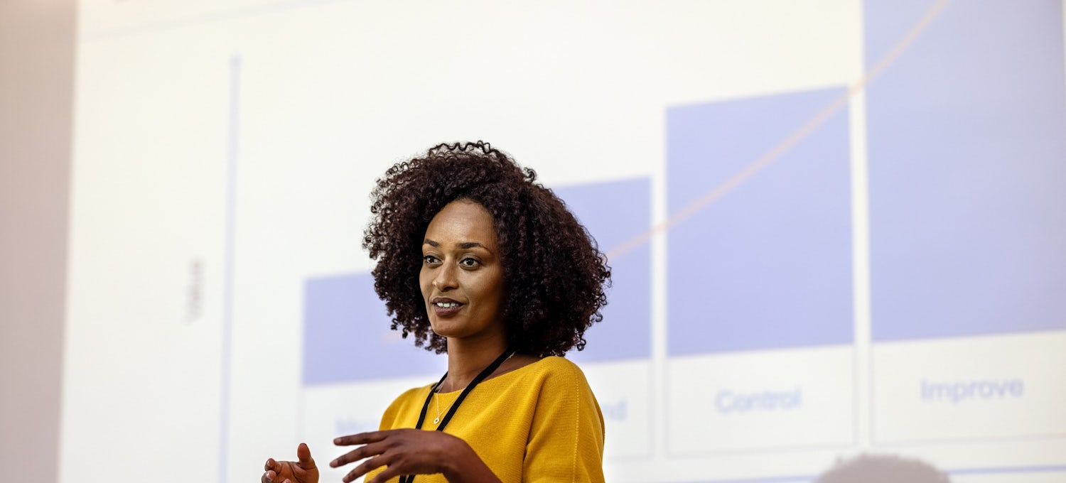 [Featured Image]: The marketing manager, wearing a yellow top, is making a PowerPoint presentation.