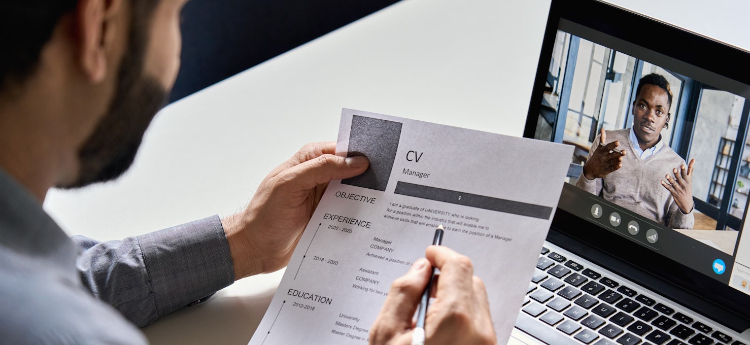 [Featured image] A recruiter holds a printed CV and interviews a candidate virtually via laptop for a role in human resource management.