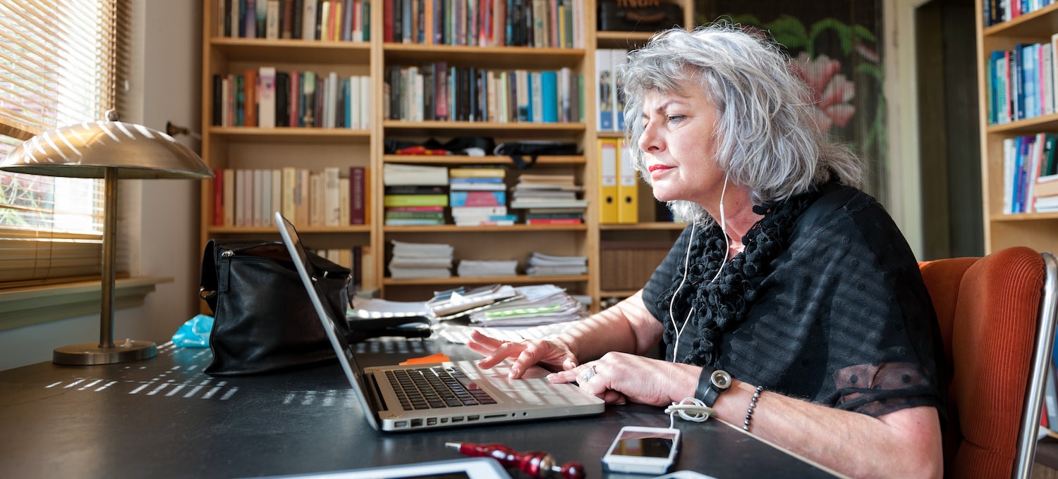 [Featured image] A professor writes a letter of recommendation on her laptop in an office filled with bookshelves.