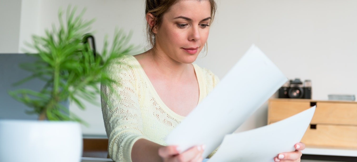 [Featured image] A woman in a pale yellow sweater sits at a table and looks over a two-page resume. There's a plant on the table in front of her.
