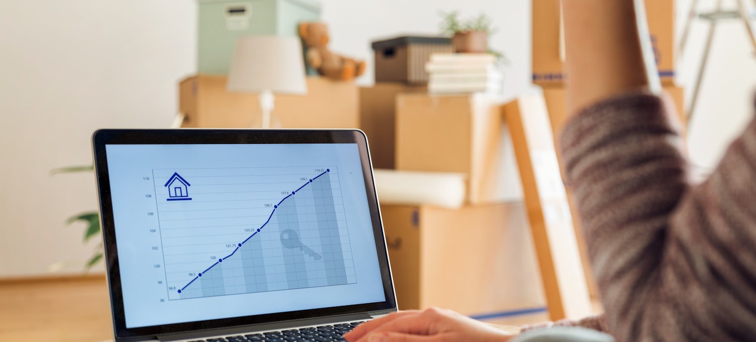 [Featured Image] A woman who is moving into a new home looks at a real estate line graph on a laptop.