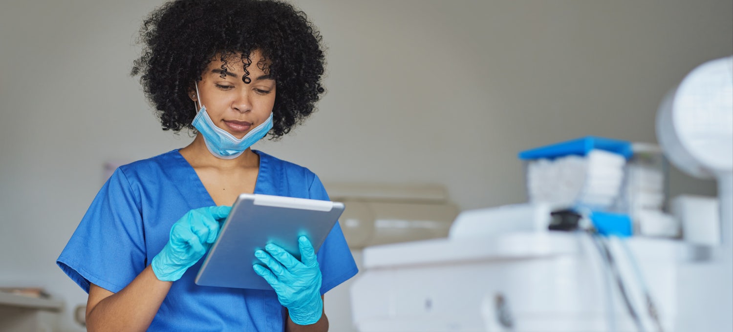 [Featured Image] A dental hygienist looks at a tablet. 