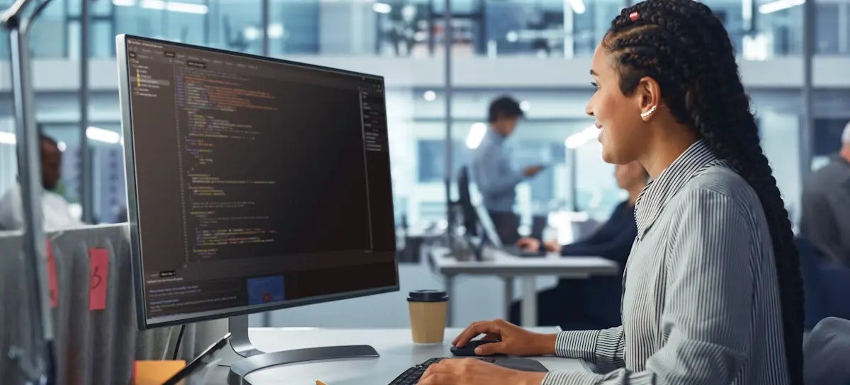 [Featured Image] A person works at a desktop computer in an office, comparing Java and C++.