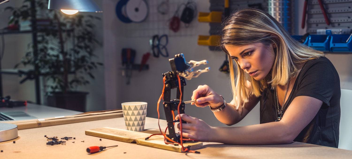 [Featured image] A master's in physics degree candidate uses a screwdriver to adjust a robotic device she's working on. 