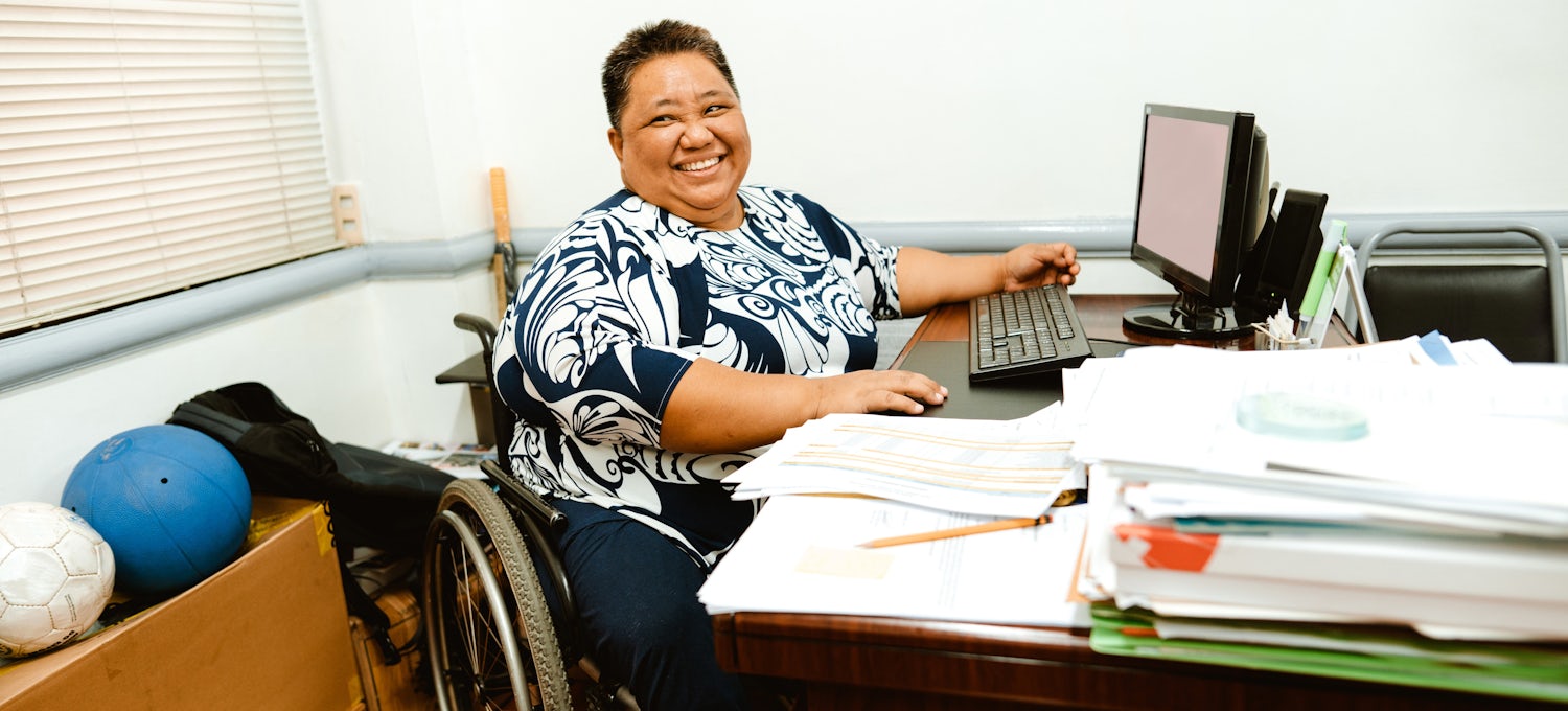 [Featured image] A financial advisor in a wheelchair sits in front of a computer with a stack of financial reports in front of her.