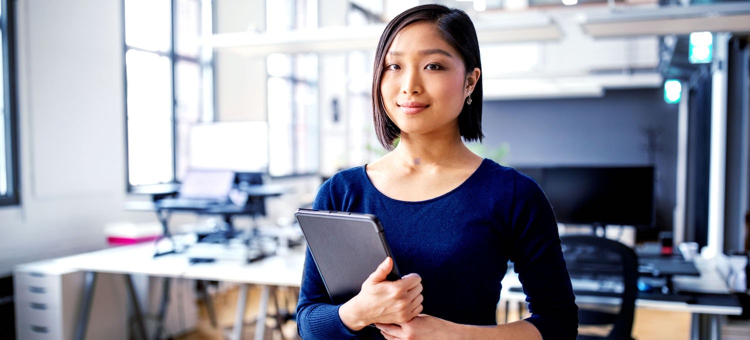 [Featured image] A young Asian woman holding a tablet stands in an empty office. 