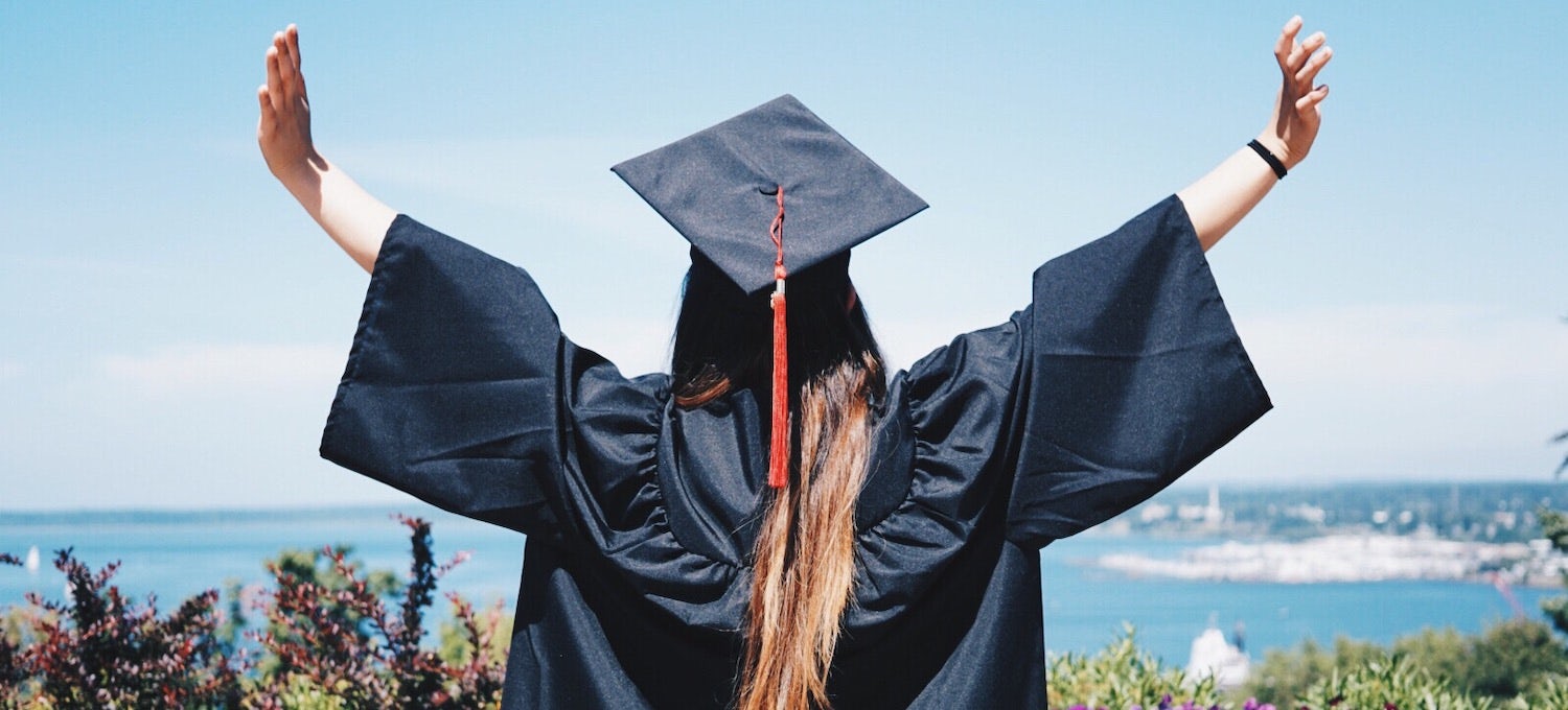 [Imagen destacada] Una joven graduanda de licenciatura, con toga y birrete, levanta los brazos en señal de celebración. 