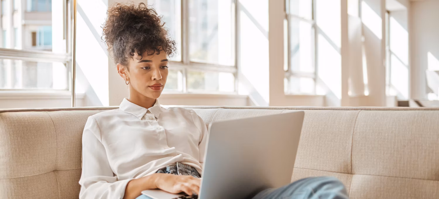 [Featured Image} A woman interested in an IT career relaxes on a sofa and searches on her laptop, "What is the easiest IT certificate to get."