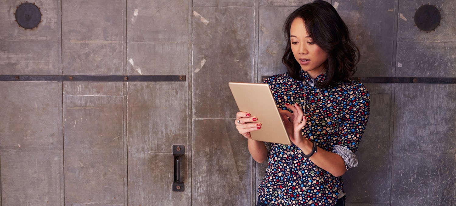 [Featured image] A person in a polka-dot shirt stands in front of a wood-paneled wall and taps the screen of their tablet.