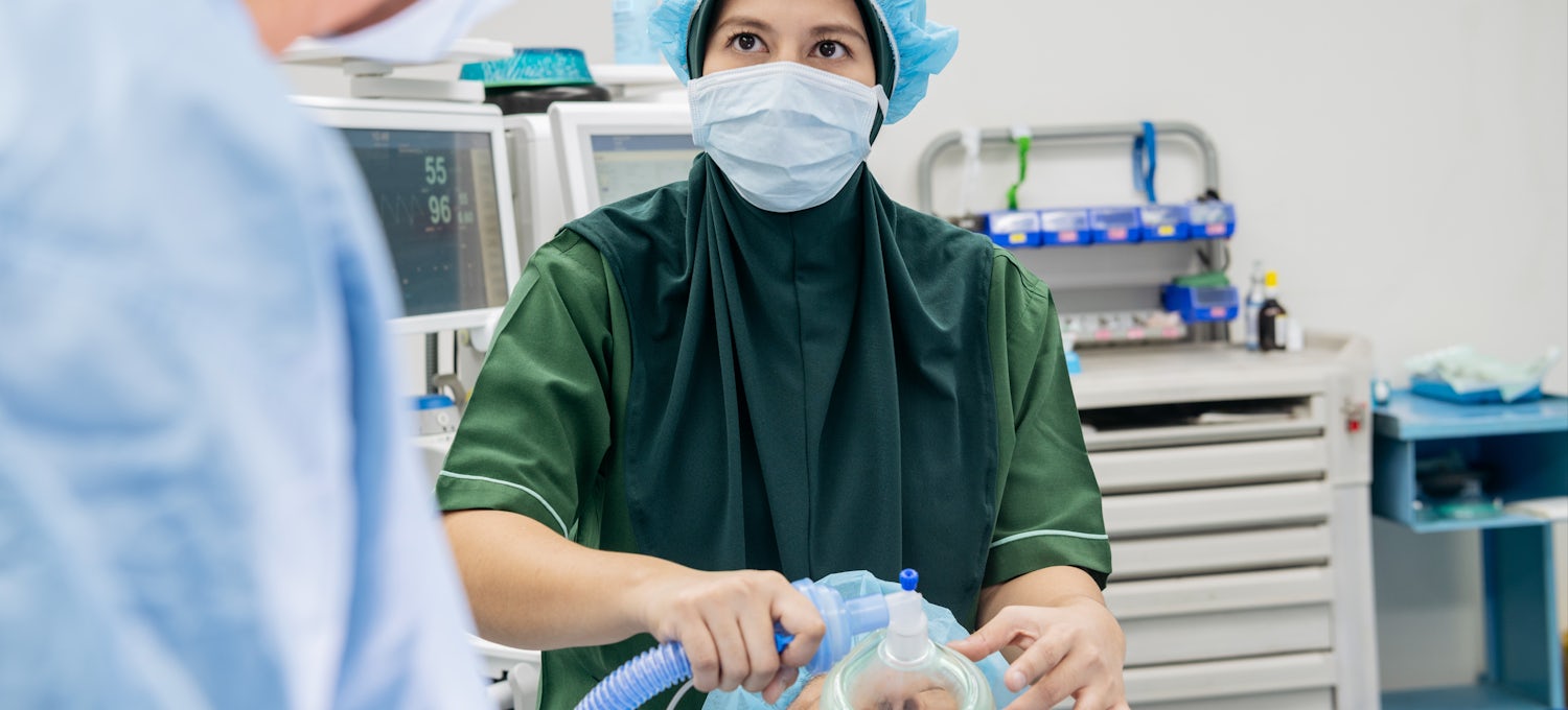 [Featured Image] A female nurse anesthetist cares for a patient in an operating room.
