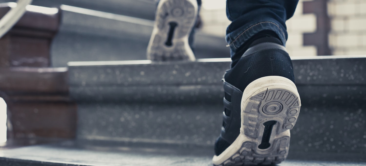 [Featured Image] Close up of someone's feet with sneakers walking up stairs