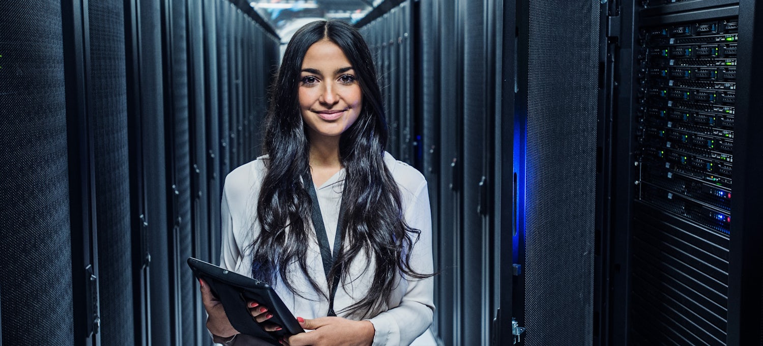 [Featured Image] A woman stands in a server room holding a tablet.