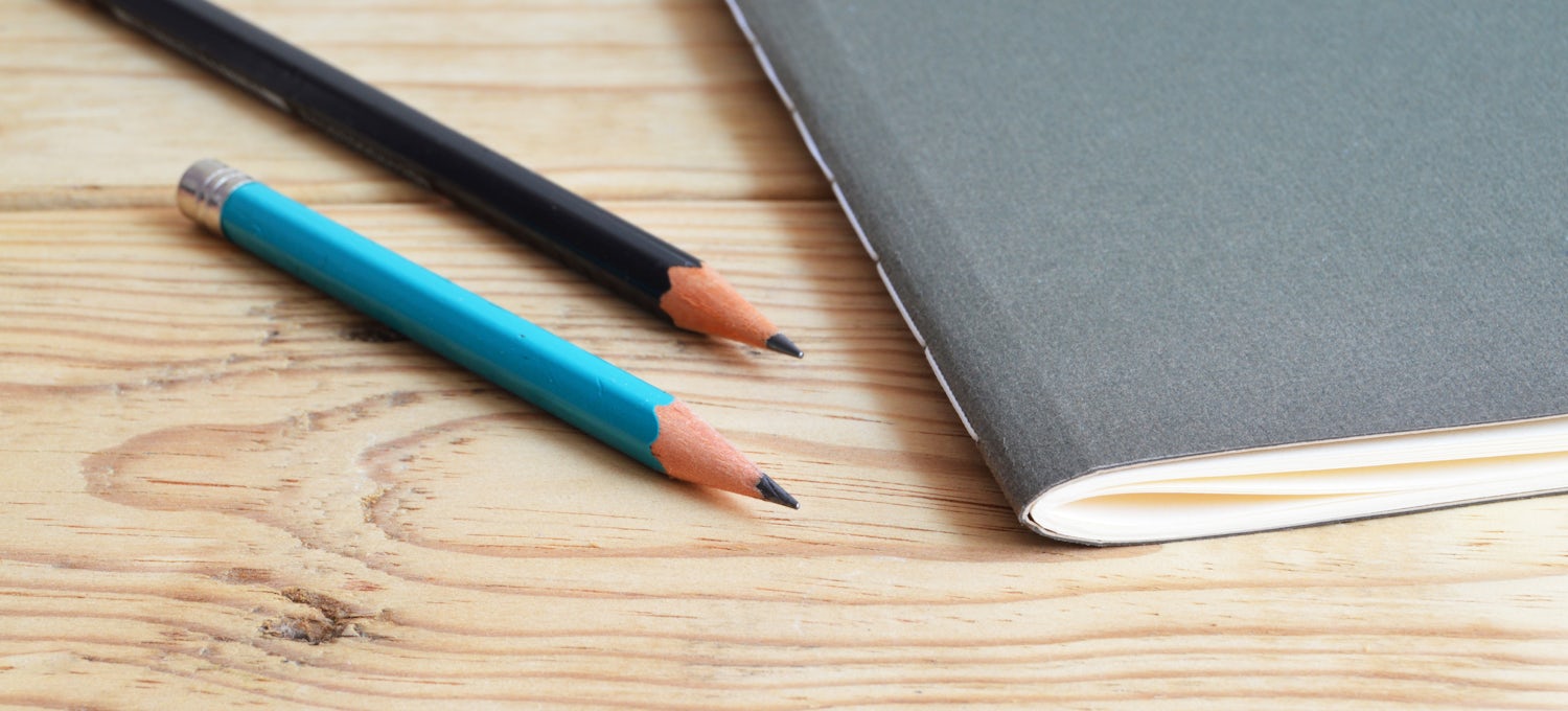 [Featured image] A dark gray notebook and two pencils sit on a wood surface.