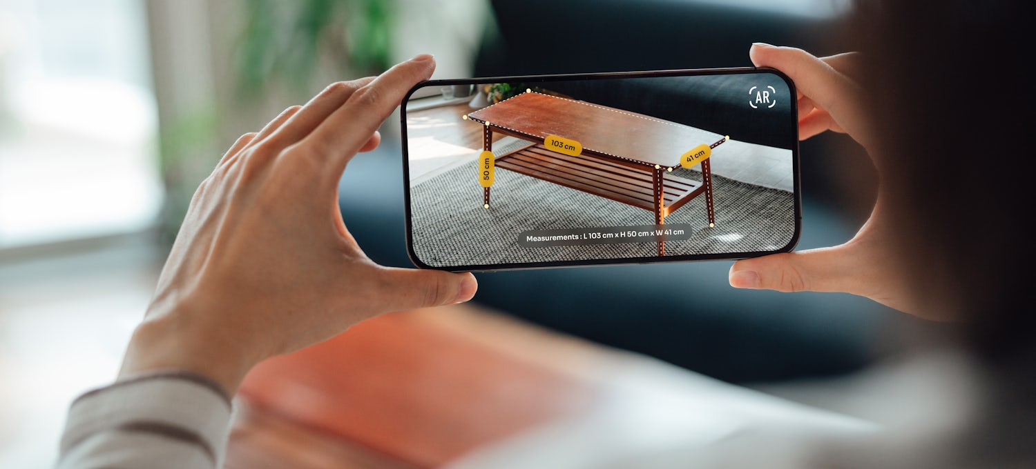 [Featured Image] A woman uses her smartphone to shop online for furniture and see how it would look in her house, one of many augmented reality examples. 