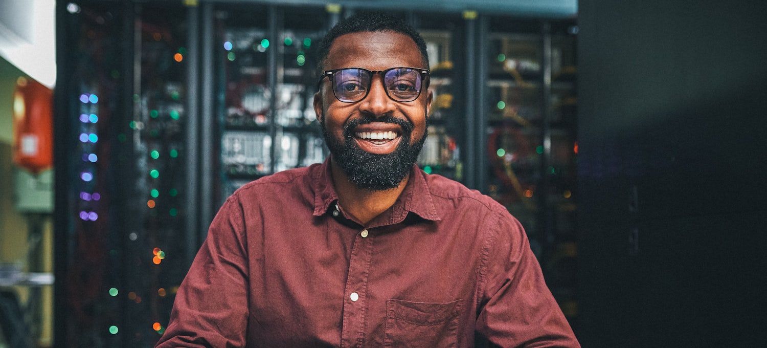 [Featured Image] A machine learning engineer who works with a form of a  natural processing language wears a red button-down shirt and sits in a server storage room.