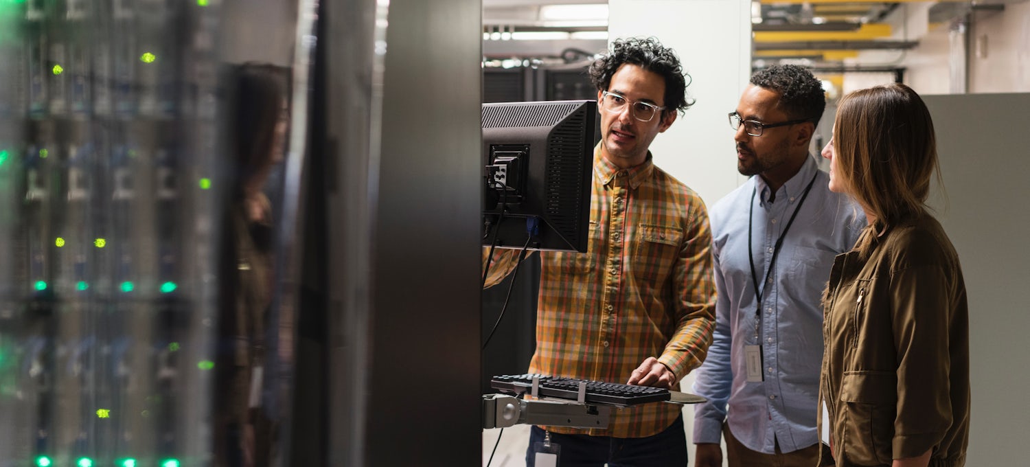 [Featured Image] A group of machine learning engineers stand around a computer, analyzing a machine learning application in the technology field.