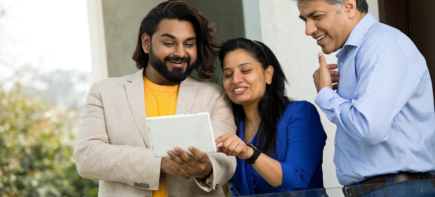 [Featured image] An HR team looks at a document on tablet while standing in an office hallway.