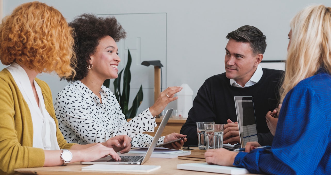 [Featured image] Two people from the marketing team meet with two people from the sales team at a conference table.