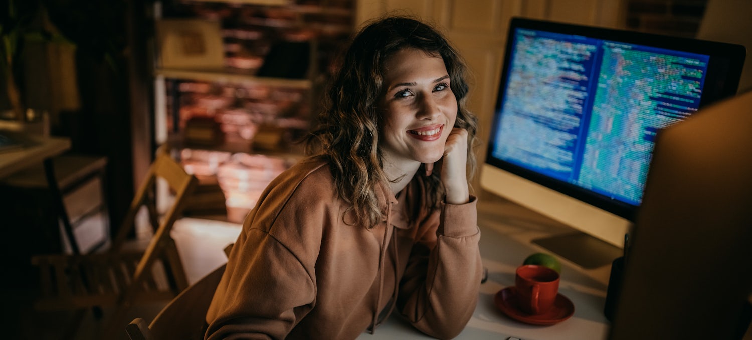 [Imagen destacada] Una ingeniero en redes sentada frente a su estación de trabajo sonríe a la cámara.