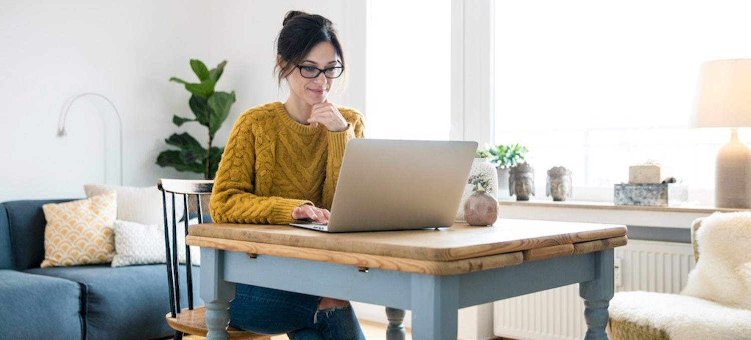 [Featured image] A woman wearing a yellow sweater and glasses sits at laptop working on an online degree course