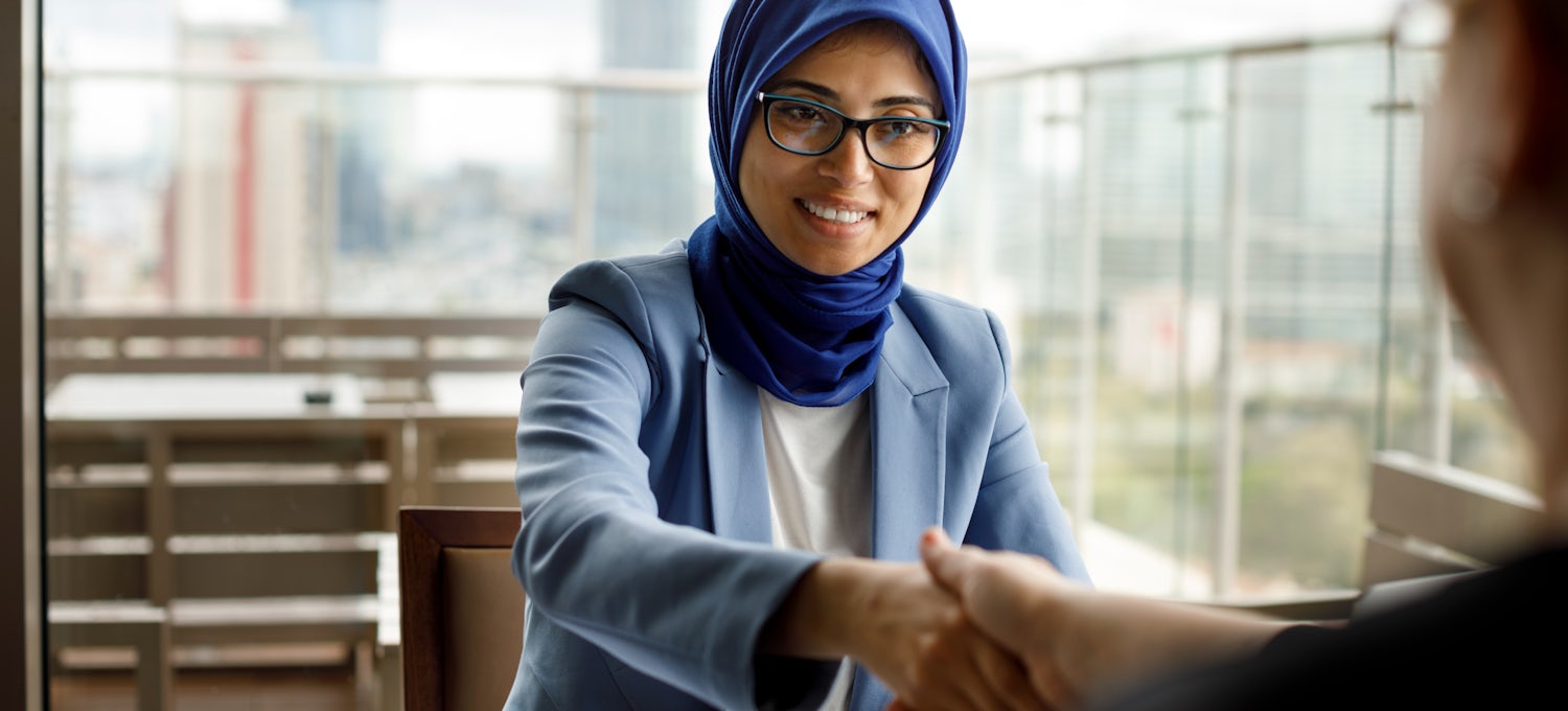 [Featured Image] A woman in a hijab shakes hands across a restaurant table. 