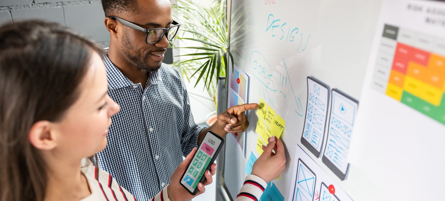 [Featured Image] A man and woman map out a mobile app design on a whiteboard.