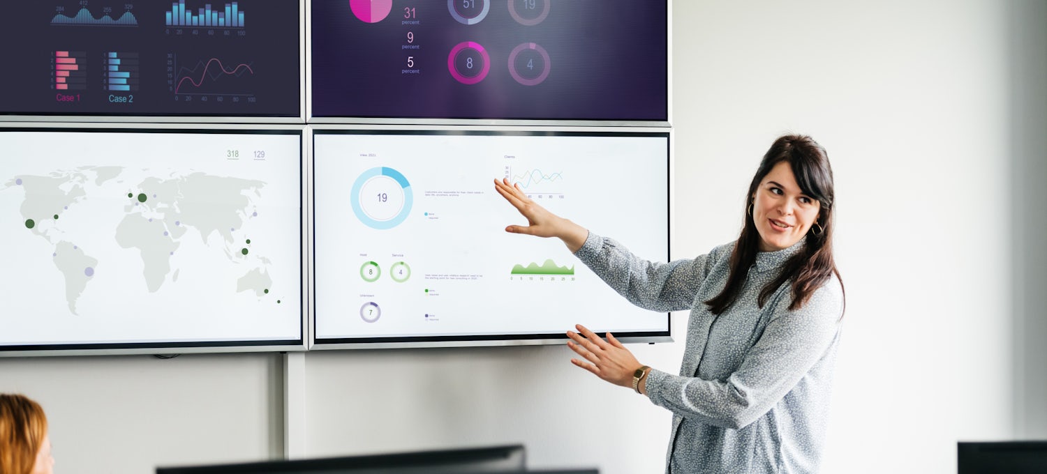 [Featured image]  Quality assurance test case writer demonstrates test case examples on a grid of four wall-mounted monitors.
