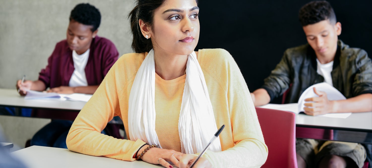 [Featured image] A woman in a yellow shirt and scarf sits at a desk preparing to take a college entrance exam.