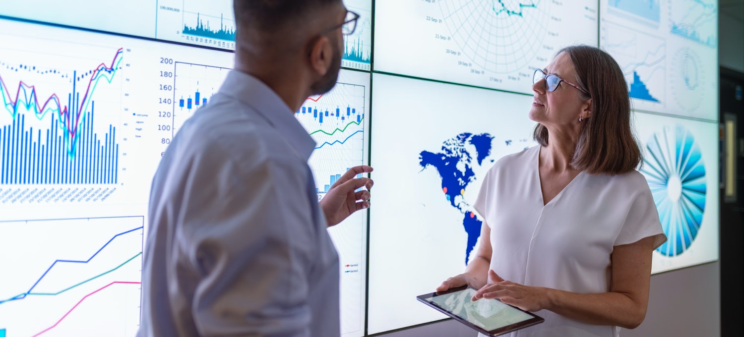 [Featured image] Two business analysts look at Tableau data visualizations on large monitors.