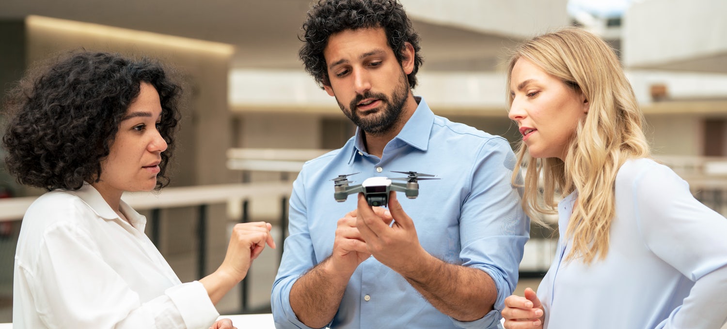 [Featured Image] Three engineers discuss simultaneous localization and mapping while looking at a drone.  