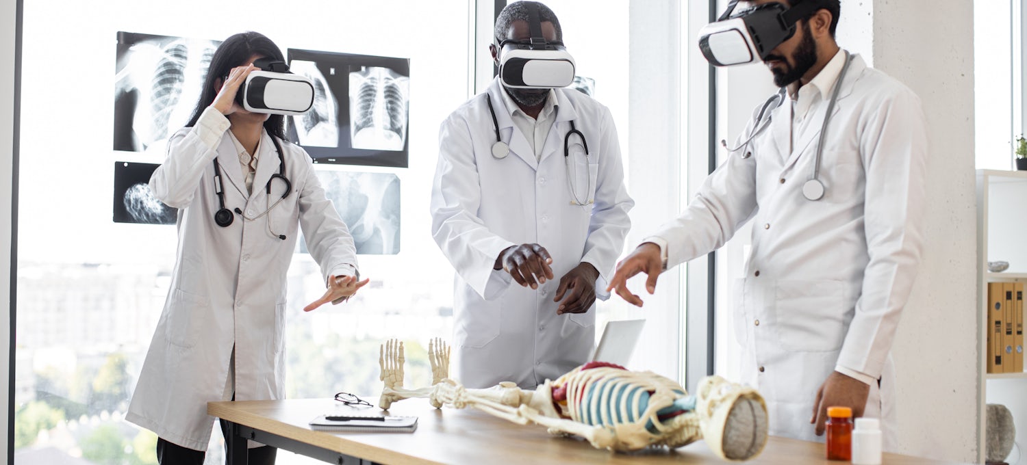 [Featured Image] A group of doctors uses mixed reality to study the human skeletal system using a skeleton model and VR goggles.