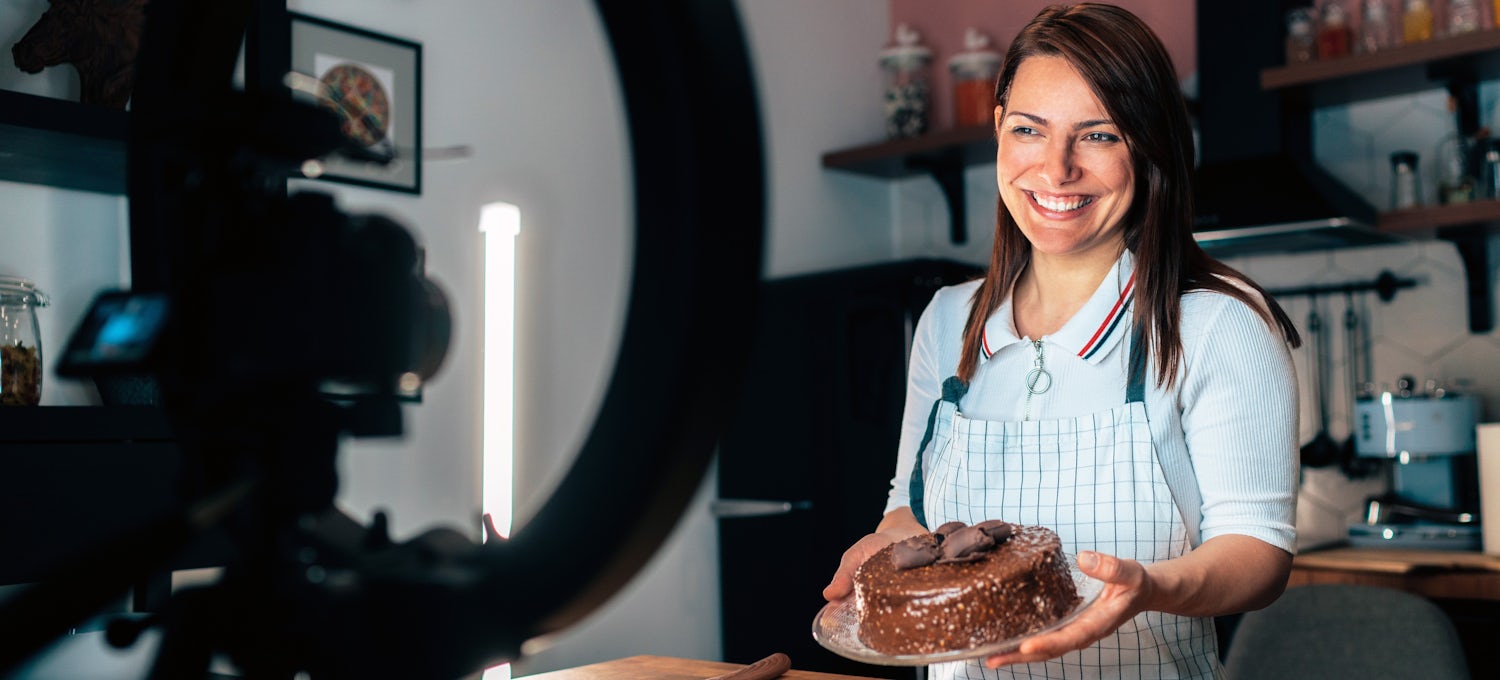 [Featured image] A food influencer holds a cake and smiles in front of a video camera.