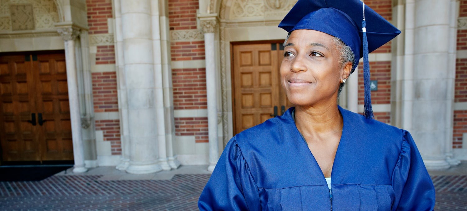 [Featured image] A woman in a blue cap and gown stands outside a university building after graduating with a business degree. 