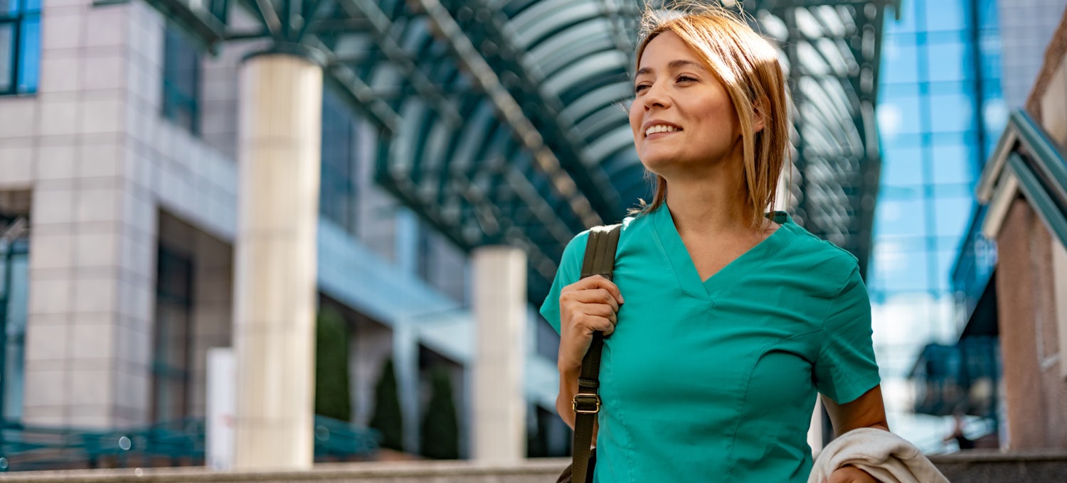 [Featured image] A travel nurse in teal scrubs walks through an airport.