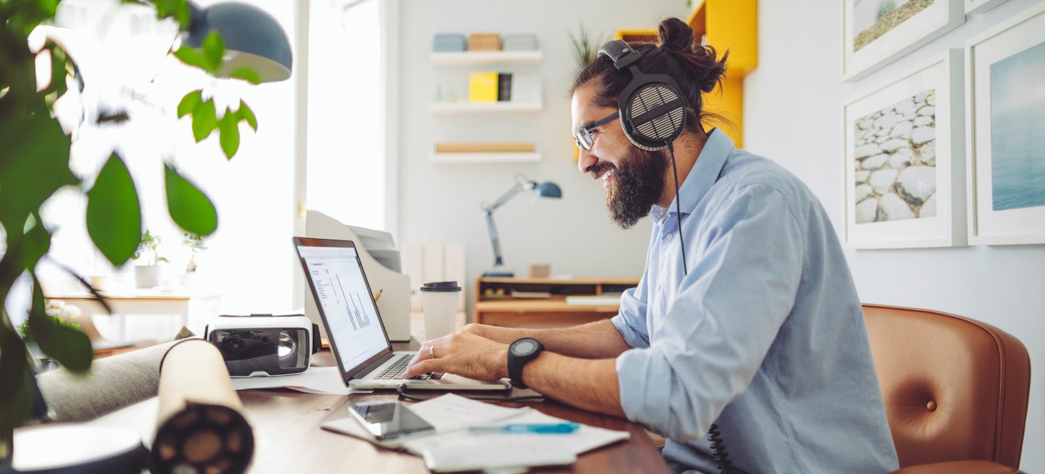 [Featured image] A UX engineer in a blue shirt works on a laptop and wears over-the-ear headphones.