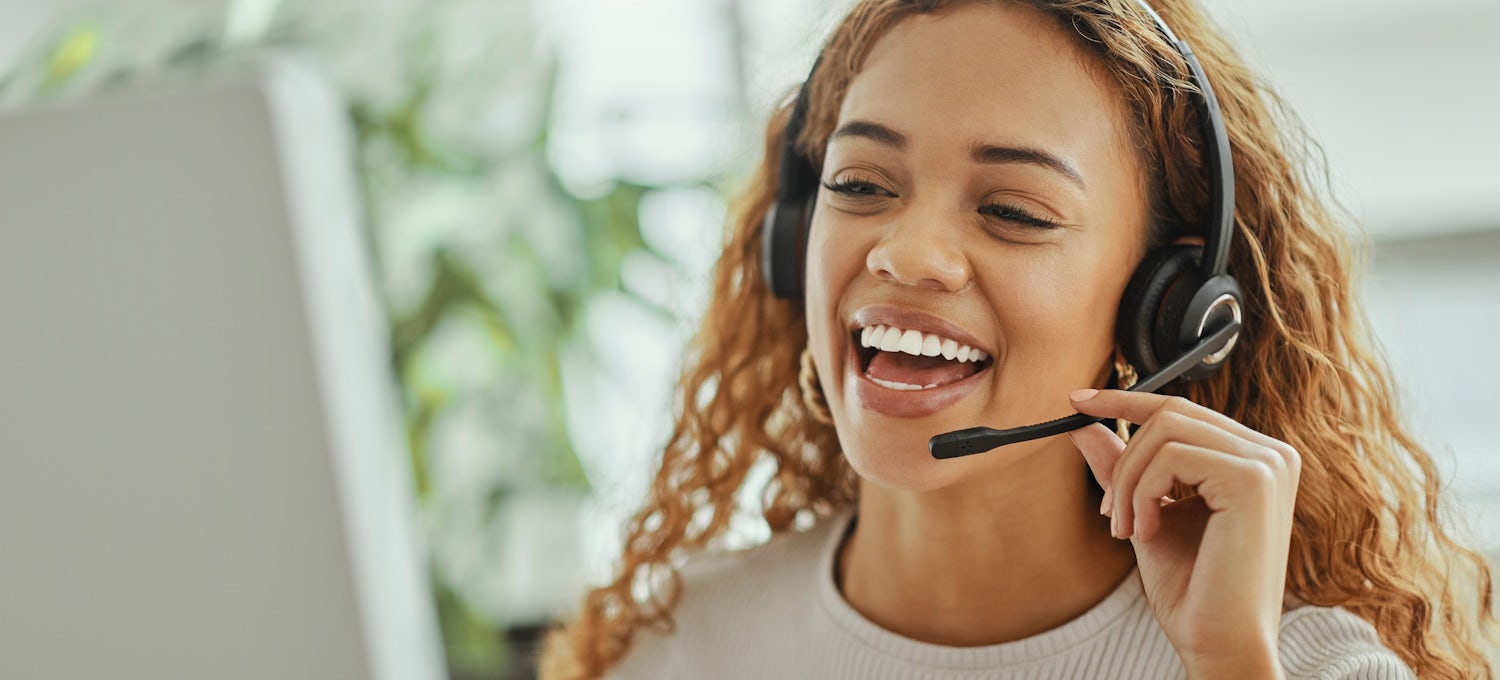 [Featured Image] A smiling customer service representative wearing a headset speaks to a customer on the phone when ChatGPT is not able to answer their questions.
