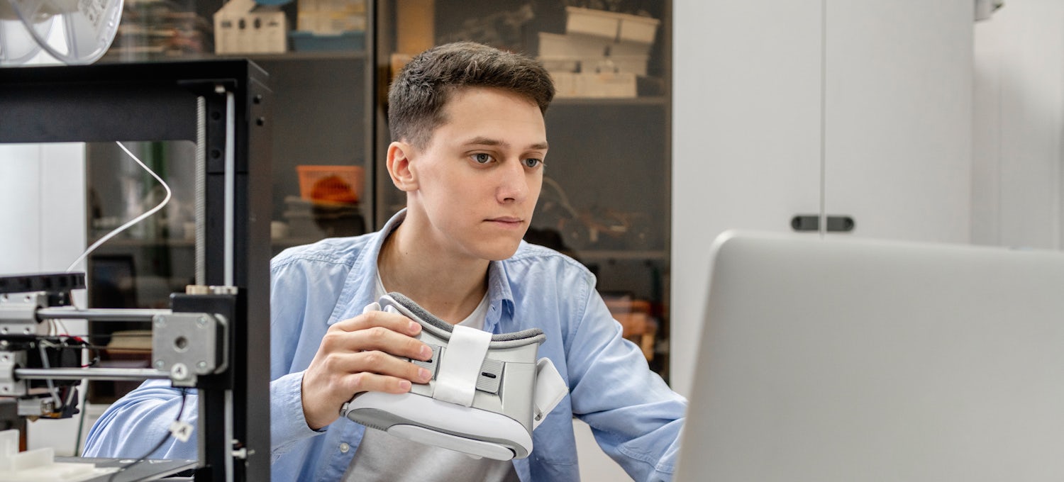 [Featured image] A data science student in a blue shirt and holding goggles works on his computer.