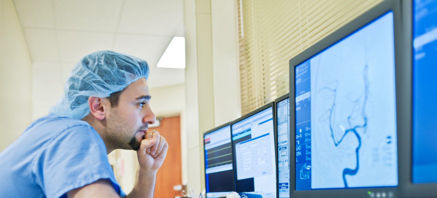 [Featured Image]:  A health care worker, working at his desktop computer, is analyzing the charts of a patient.