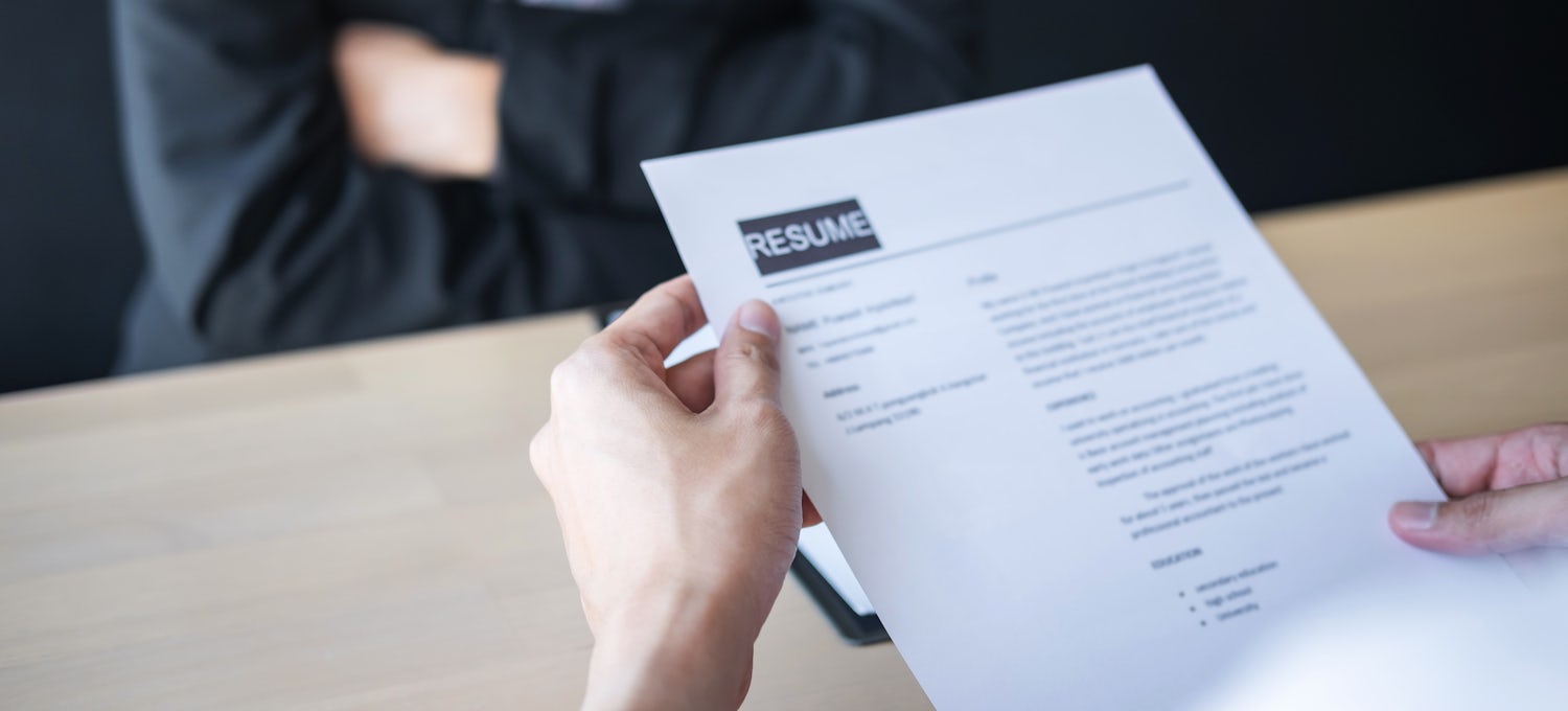 [Featured images] A hiring manager's hands holding a paper resume over a desk