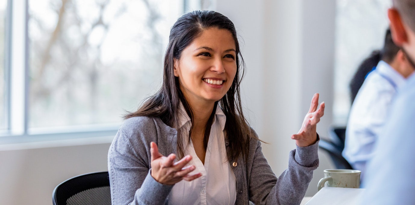 [Featured image] A young woman working in healthcare administration speaking animatedly with her colleague.