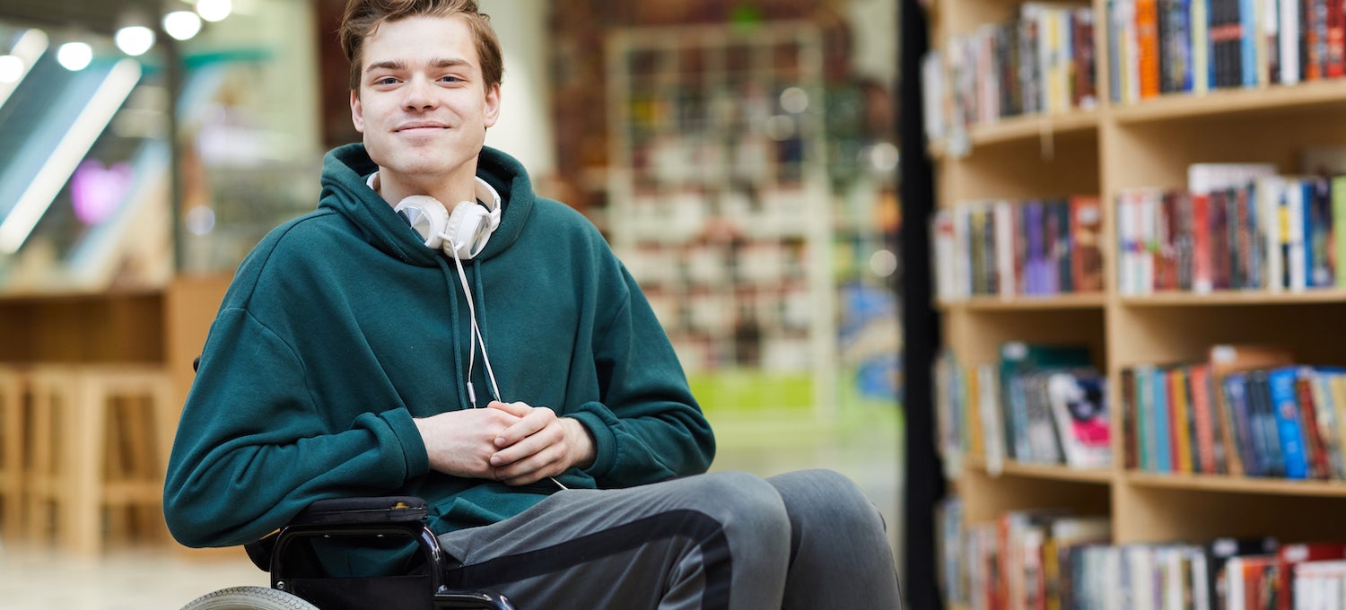 [Featured image] A young student in a wheelchair, wearing a teal sweatshirt and over-the-ear headphones around their neck, smiles at the camera. 