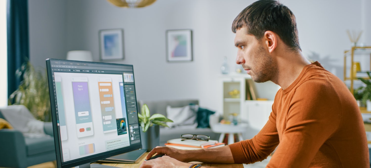 [Featured image] A UX designer in an orange long-sleeve T-shirt works on a prototype on his desktop computer.