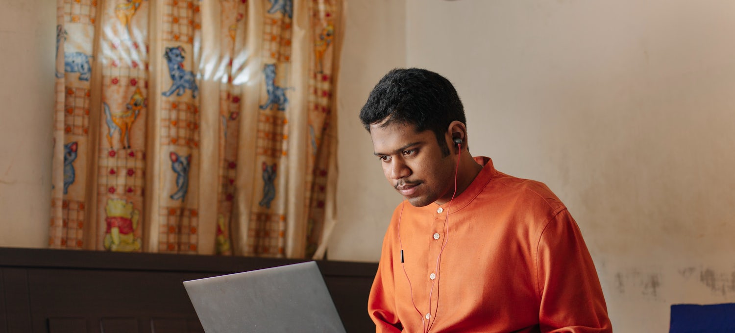 [Featured Image]:  Prospective job candidate, wearing an orange shirt and tan pants, working on a laptop computer, preparing for an interview. 