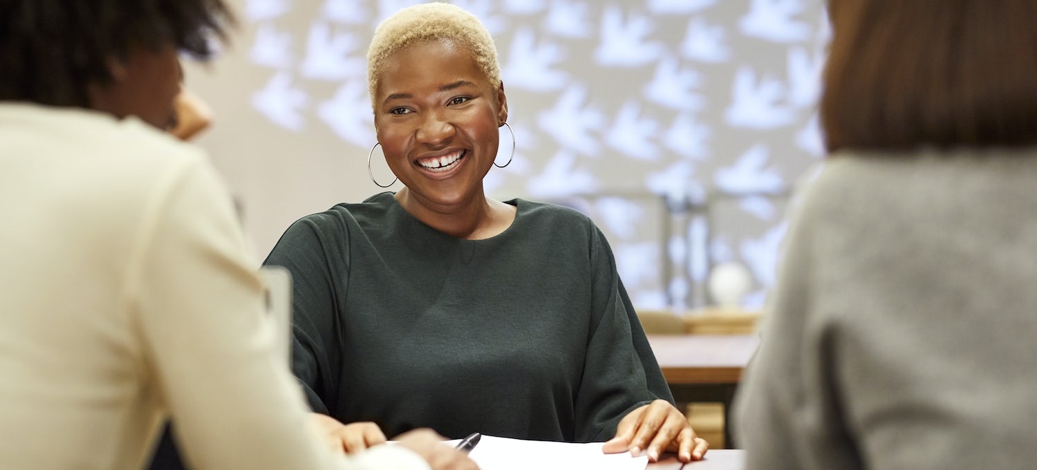 Une femme souriante aux cheveux courts et aux boucles d'oreilles est assise à une table lors d'un entretien d'embauche de designer UX