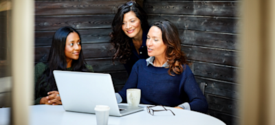 Featured image] A marketing manager meets with her team at a conference table. One woman has a laptop, glasses, and a coffee cup in front of her.