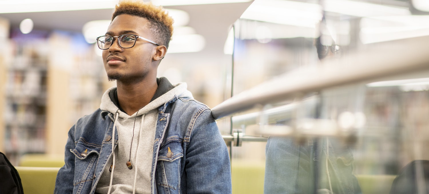 [Featured image] A young Black man with glasses sits in a library paying attention.